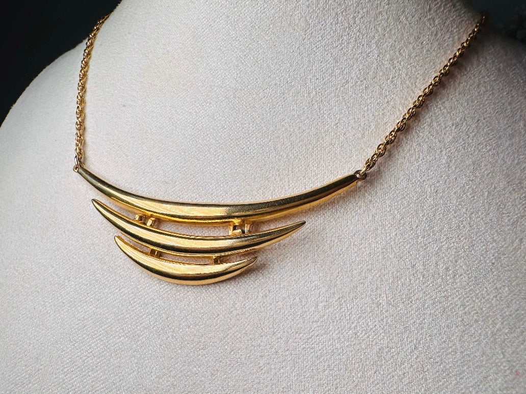 This vintage Crown Trifari triple gold bar necklace is a beauty. From the 1960s this dainty short style choker necklace looks beautiful alone or paired with others for a fantastic stack. The fine gold plated chain suspends a small gold pendant composed of 3 curved bars in graduated size- signed on back and with the signature Trifari hang tag.