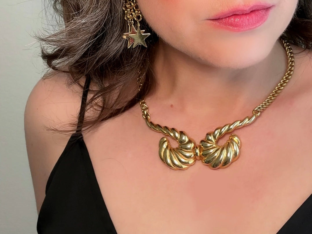 This 1970s vintage gold necklace is such a striking and unique piece. Featuring gold curb chain and a striking centerpiece of two textured gold horns. Full of vintage flair, this centerpiece is dimensional and stunning. This choker necklace is so flattering on and the perfect collar length.