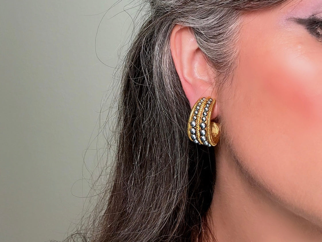 These oversized gold hoop vintage statement earrings feature two rows of chanel set dark silver pearls in graduating size, the sides are a beautiful roped texture. These dark silver pearl and gold half hoop earrings are huggie hoop style- these clip ons effortlessly add a touch of bold glam the 80s are so beloved for. A beautiful textured finish, the contrast of cool silver pearls and classic gold- these earrings are a showstopping vintage pair, in excellent condition.