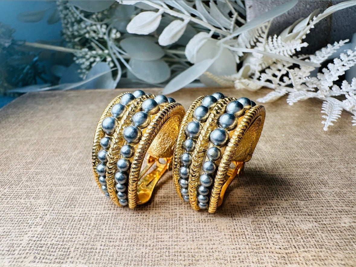These oversized gold hoop vintage statement earrings feature two rows of chanel set dark silver pearls in graduating size, the sides are a beautiful roped texture. These dark silver pearl and gold half hoop earrings are huggie hoop style- these clip ons effortlessly add a touch of bold glam the 80s are so beloved for. A beautiful textured finish, the contrast of cool silver pearls and classic gold- these earrings are a showstopping vintage pair, in excellent condition.