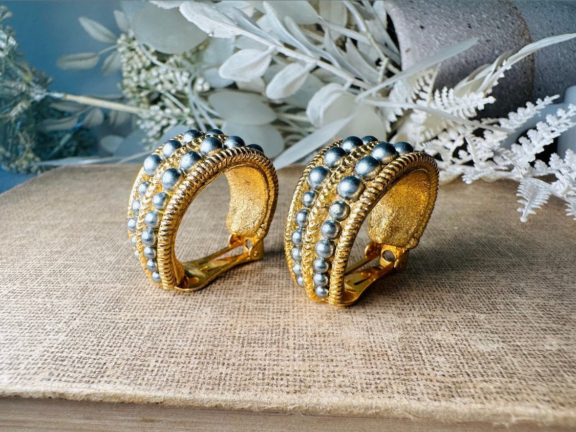 These oversized gold hoop vintage statement earrings feature two rows of chanel set dark silver pearls in graduating size, the sides are a beautiful roped texture. These dark silver pearl and gold half hoop earrings are huggie hoop style- these clip ons effortlessly add a touch of bold glam the 80s are so beloved for. A beautiful textured finish, the contrast of cool silver pearls and classic gold- these earrings are a showstopping vintage pair, in excellent condition.