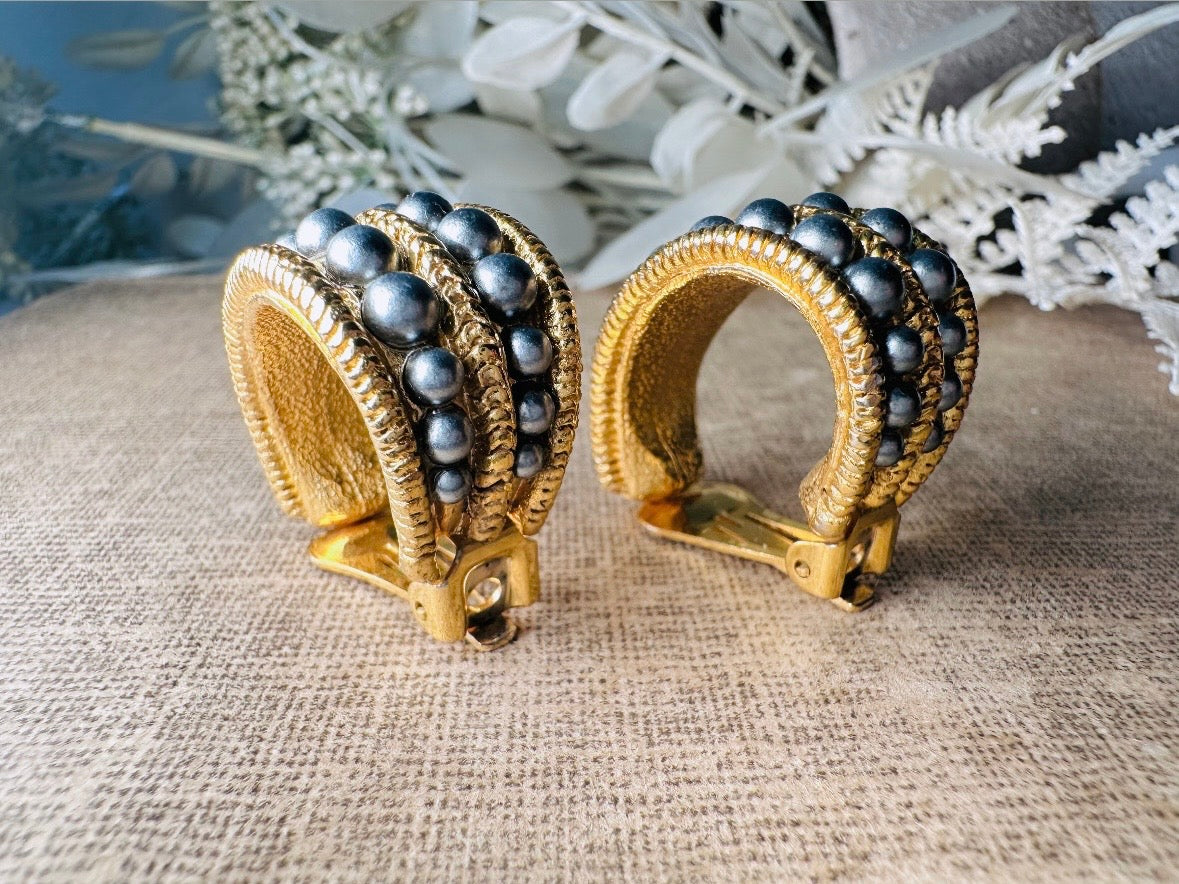 These oversized gold hoop vintage statement earrings feature two rows of chanel set dark silver pearls in graduating size, the sides are a beautiful roped texture. These dark silver pearl and gold half hoop earrings are huggie hoop style- these clip ons effortlessly add a touch of bold glam the 80s are so beloved for. A beautiful textured finish, the contrast of cool silver pearls and classic gold- these earrings are a showstopping vintage pair, in excellent condition.