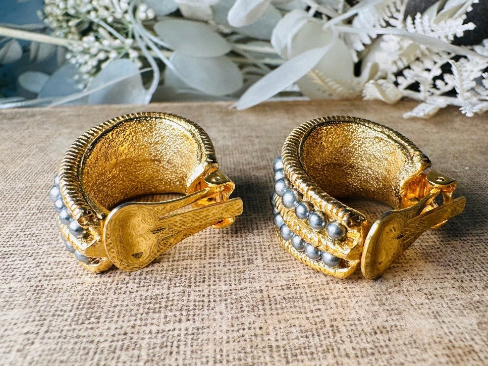 These oversized gold hoop vintage statement earrings feature two rows of chanel set dark silver pearls in graduating size, the sides are a beautiful roped texture. These dark silver pearl and gold half hoop earrings are huggie hoop style- these clip ons effortlessly add a touch of bold glam the 80s are so beloved for. A beautiful textured finish, the contrast of cool silver pearls and classic gold- these earrings are a showstopping vintage pair, in excellent condition.