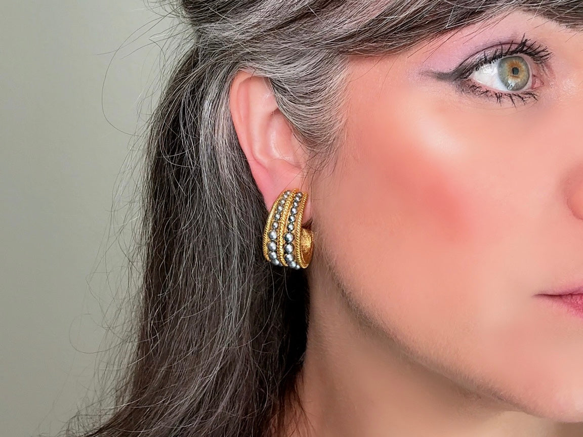 These oversized gold hoop vintage statement earrings feature two rows of chanel set dark silver pearls in graduating size, the sides are a beautiful roped texture. These dark silver pearl and gold half hoop earrings are huggie hoop style- these clip ons effortlessly add a touch of bold glam the 80s are so beloved for. A beautiful textured finish, the contrast of cool silver pearls and classic gold- these earrings are a showstopping vintage pair, in excellent condition.