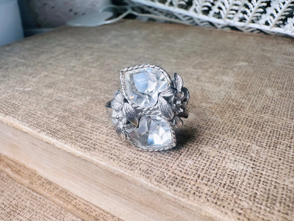 This beautiful sparkling vintage ring features two diamond heart rhinestones flanked by a flower and leaves on each side. Made in the 70's this sparkly ring is a wonderfully thoughtful vintage gift for an April birthday. Great vintage condition, very minor wear, no flaws to note- please see pics.
Dimensions: size 9 max and adjustable to be smaller