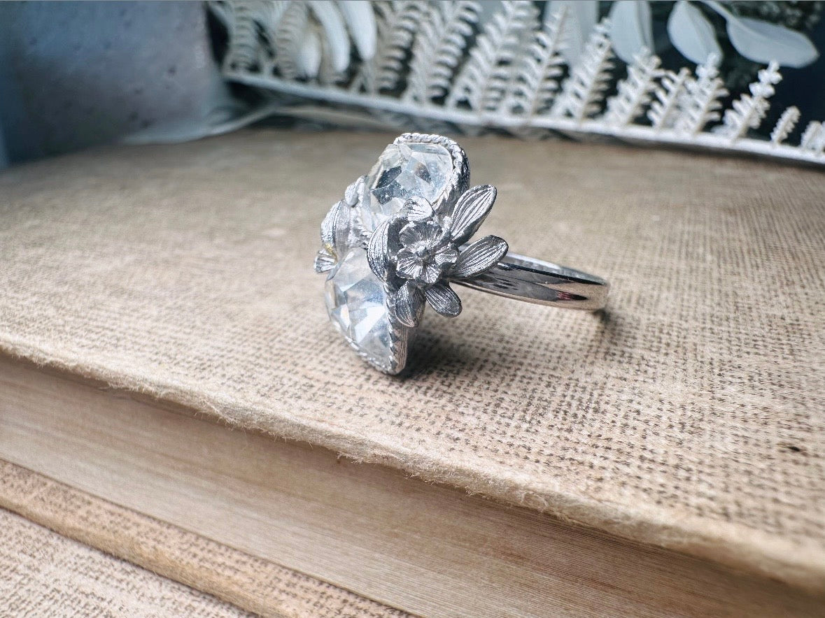 This beautiful sparkling vintage ring features two diamond heart rhinestones flanked by a flower and leaves on each side. Made in the 70's this sparkly ring is a wonderfully thoughtful vintage gift for an April birthday. Great vintage condition, very minor wear, no flaws to note- please see pics.
Dimensions: size 9 max and adjustable to be smaller