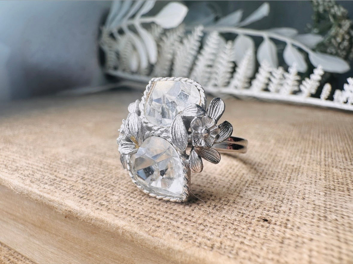 This beautiful sparkling vintage ring features two diamond heart rhinestones flanked by a flower and leaves on each side. Made in the 70's this sparkly ring is a wonderfully thoughtful vintage gift for an April birthday. Great vintage condition, very minor wear, no flaws to note- please see pics.
Dimensions: size 9 max and adjustable to be smaller
