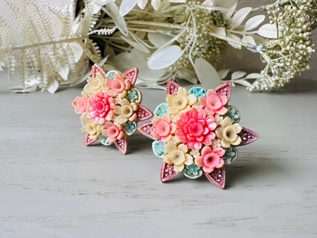 These vintage 1950s Japanese floral celluloid earrings are so colorful. Carved celluloid bursting with sakura blossoms and flowers, these earrings are on the larger side and are painted with a beautiful pearlized pink, blue and light cream. The star-shaped base and raised beaded edges are also characteristic of vintage Japanese celluloid jewelry. They are 1.5" in size.