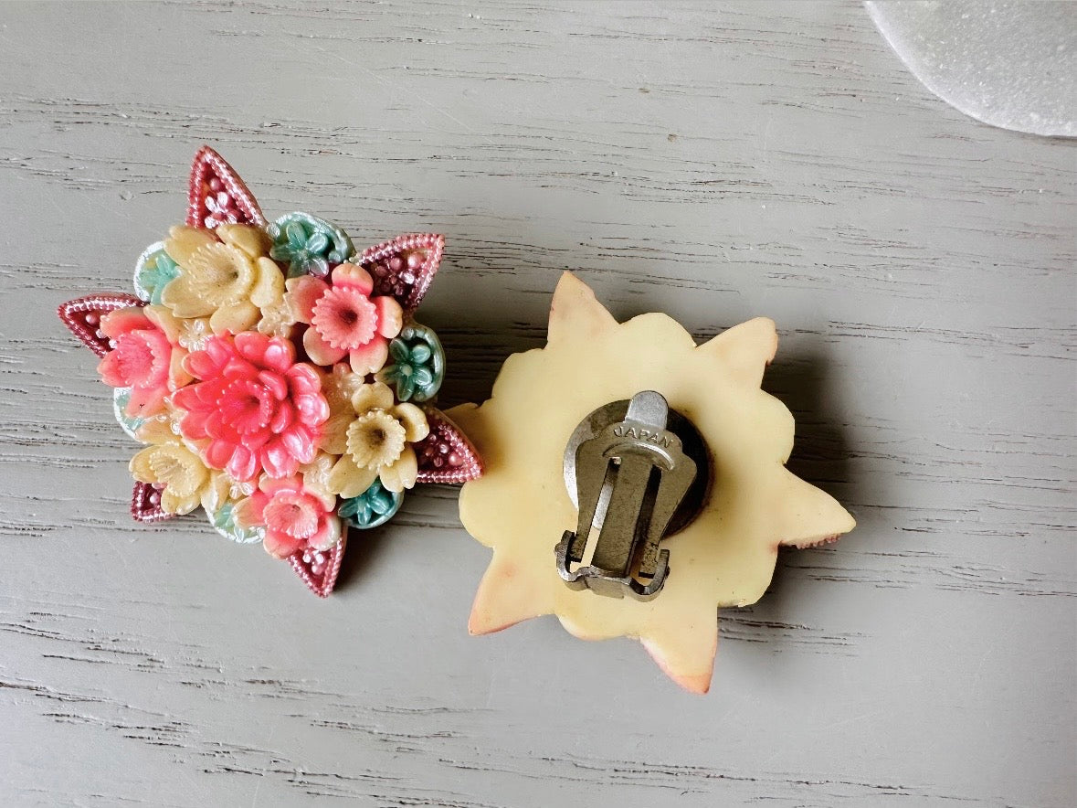 These vintage 1950s Japanese floral celluloid earrings are so colorful. Carved celluloid bursting with sakura blossoms and flowers, these earrings are on the larger side and are painted with a beautiful pearlized pink, blue and light cream. The star-shaped base and raised beaded edges are also characteristic of vintage Japanese celluloid jewelry. They are 1.5" in size.