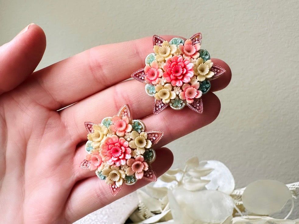 Held in hand for size reference. These vintage 1950s Japanese floral celluloid earrings are so colorful. Carved celluloid bursting with sakura blossoms and flowers, these earrings are on the larger side and are painted with a beautiful pearlized pink, blue and light cream. The star-shaped base and raised beaded edges are also characteristic of vintage Japanese celluloid jewelry. They are 1.5" in size.