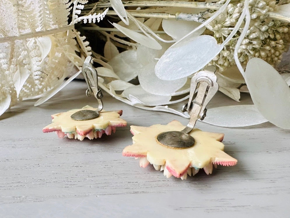 Showing the paddle back clip ons. These vintage 1950s Japanese floral celluloid earrings are so colorful. Carved celluloid bursting with sakura blossoms and flowers, these earrings are on the larger side and are painted with a beautiful pearlized pink, blue and light cream. The star-shaped base and raised beaded edges are also characteristic of vintage Japanese celluloid jewelry. They are 1.5" in size.