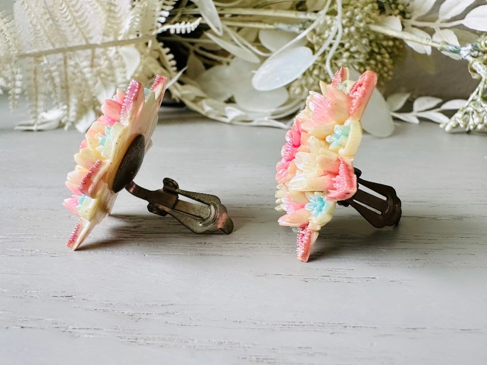 These vintage 1950s Japanese floral celluloid earrings are so colorful. Carved celluloid bursting with sakura blossoms and flowers, these earrings are on the larger side and are painted with a beautiful pearlized pink, blue and light cream. The star-shaped base and raised beaded edges are also characteristic of vintage Japanese celluloid jewelry. They are 1.5" in size. side view