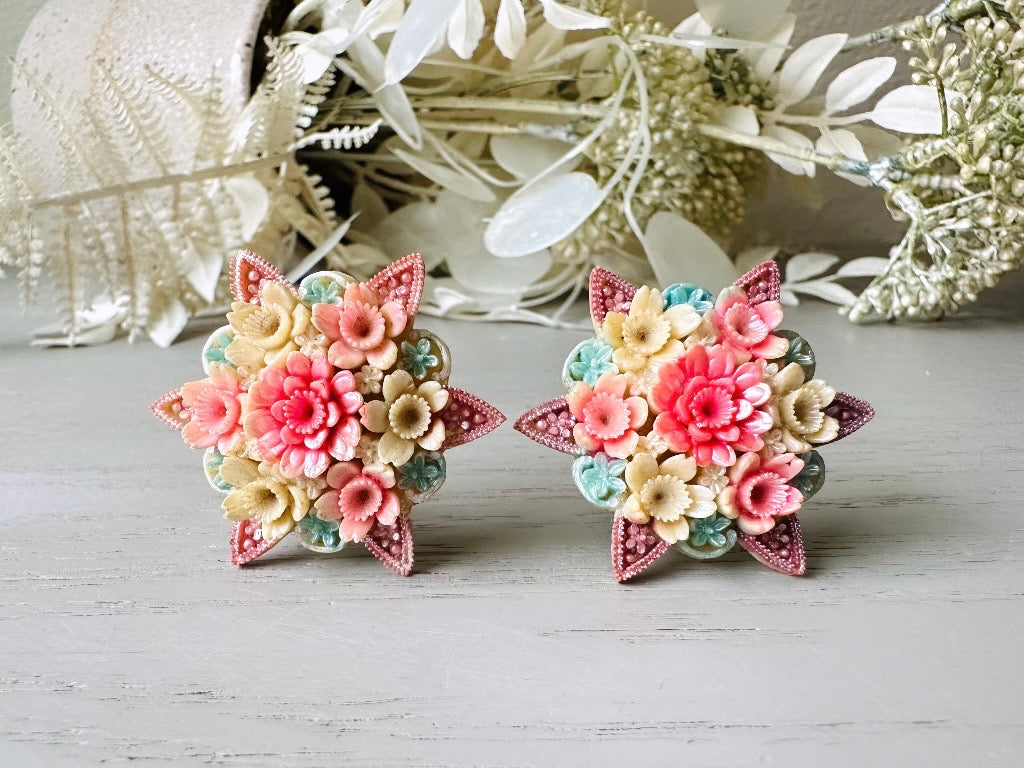 These vintage 1950s Japanese floral celluloid earrings are so colorful. Carved celluloid bursting with sakura blossoms and flowers, these earrings are on the larger side and are painted with a beautiful pearlized pink, blue and light cream. The star-shaped base and raised beaded edges are also characteristic of vintage Japanese celluloid jewelry. They are 1.5" in size.