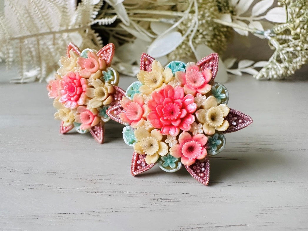 These vintage 1950s Japanese floral celluloid earrings are so colorful. Carved celluloid bursting with sakura blossoms and flowers, these earrings are on the larger side and are painted with a beautiful pearlized pink, blue and light cream. The star-shaped base and raised beaded edges are also characteristic of vintage Japanese celluloid jewelry. They are 1.5" in size.