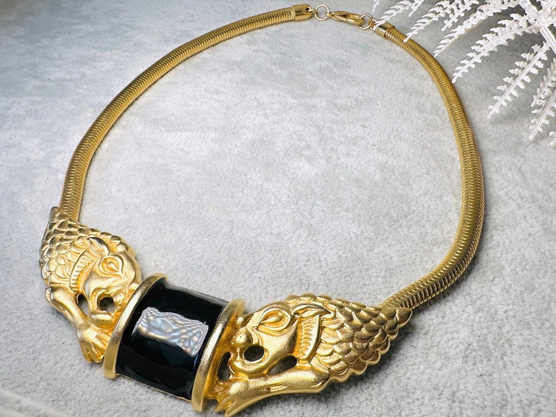 This bold vintage Etruscan style double lion necklace is truly incredible. Featuring two intricate sculptural gold lions on either side of a black enamel focal. This vintage collar necklace is the height of 80s glam, with its contrasting shiny black enamel and matte satin gold components. Wide snake chain and an oversized clasp complete this sensational necklace.