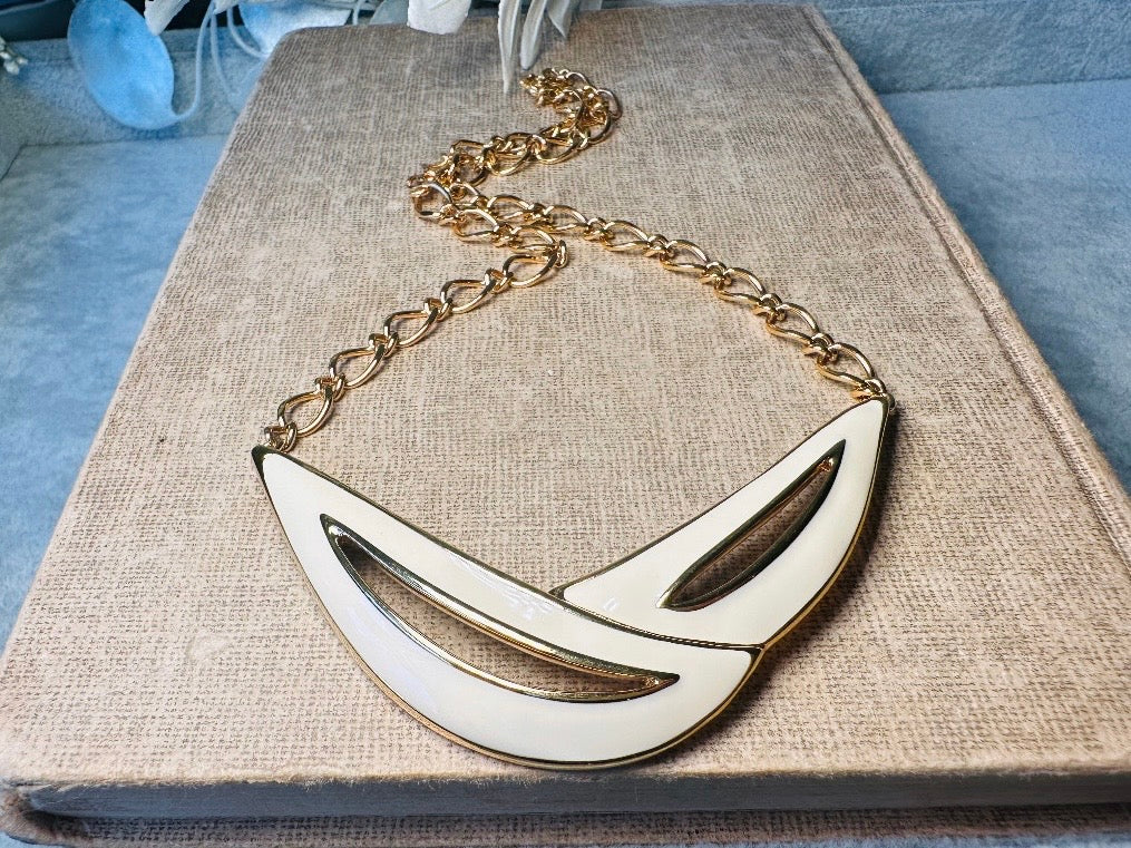 This cream and gold Monet vintage necklace is a striking classic. The focal pendant is an abstract asymmetrical crescent in gold with creamy enamel and sleek cut outs. This vintage designer necklace features gold cable chain and a signature Monet clasp and tag, also signed on back. This is a spectacular modernist jewelry piece to layer and easily goes with a variety of styles. Monet is renowned and well loved for beautiful jewelry that has stood the test of time. Excellent vintage condition, no flaws to not