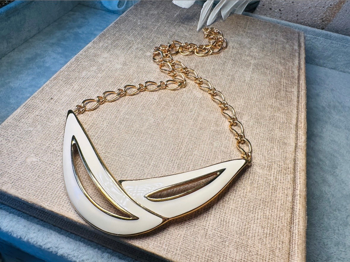 This cream and gold Monet vintage necklace is a striking classic. The focal pendant is an abstract asymmetrical crescent in gold with creamy enamel and sleek cut outs. This vintage designer necklace features gold cable chain and a signature Monet clasp and tag, also signed on back. This is a spectacular modernist jewelry piece to layer and easily goes with a variety of styles. Monet is renowned and well loved for beautiful jewelry that has stood the test of time. Excellent vintage condition, no flaws to not