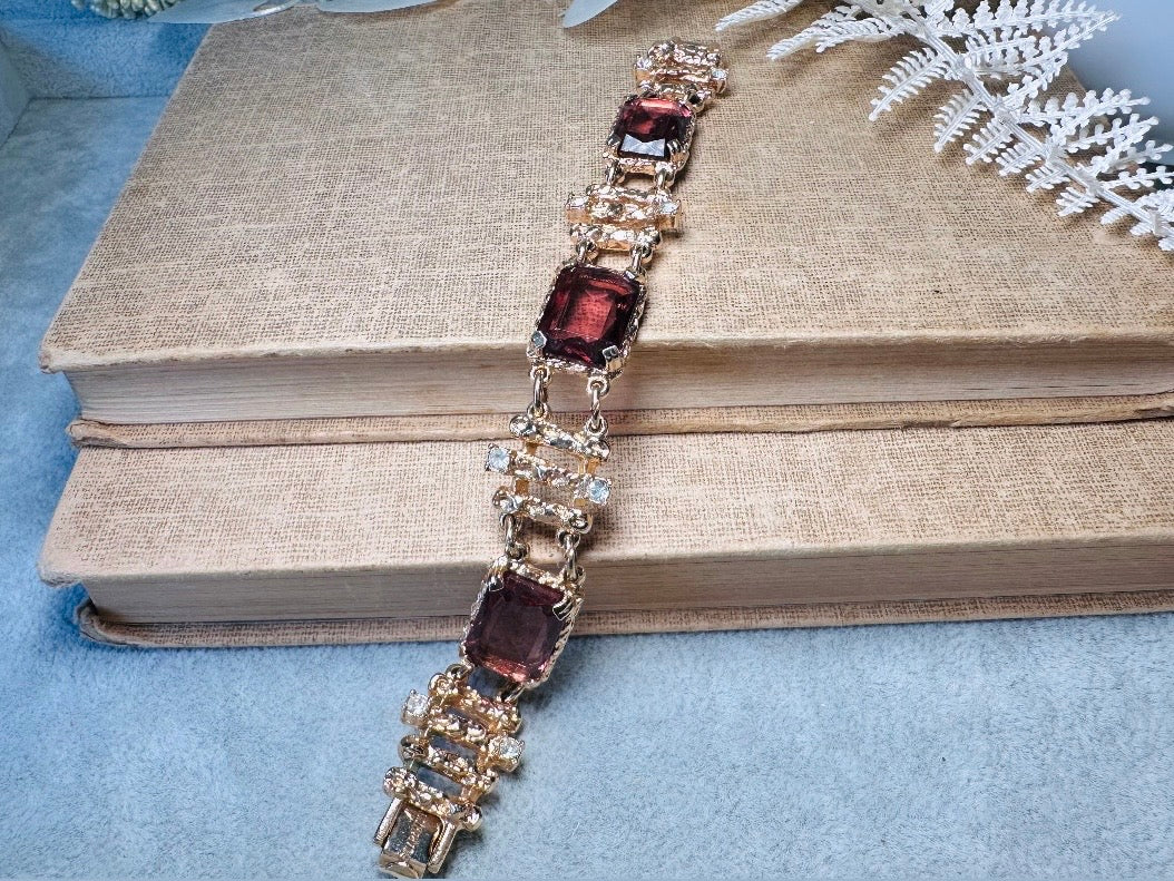 This 1970s faux amethyst vintage statement bracelet is gorgeous. Featuring three large smoky purple amethyst emerald cut stones prong set in gold. The setting is absolutely gorgeous in it's molten details- with a framed backing so the light can reflect through. Between each stone are golden branches in a brutalist style with small crystal accents. Absolutely beautiful vintage piece. Marked Sarah Coventry from 1973 Twilight collection.