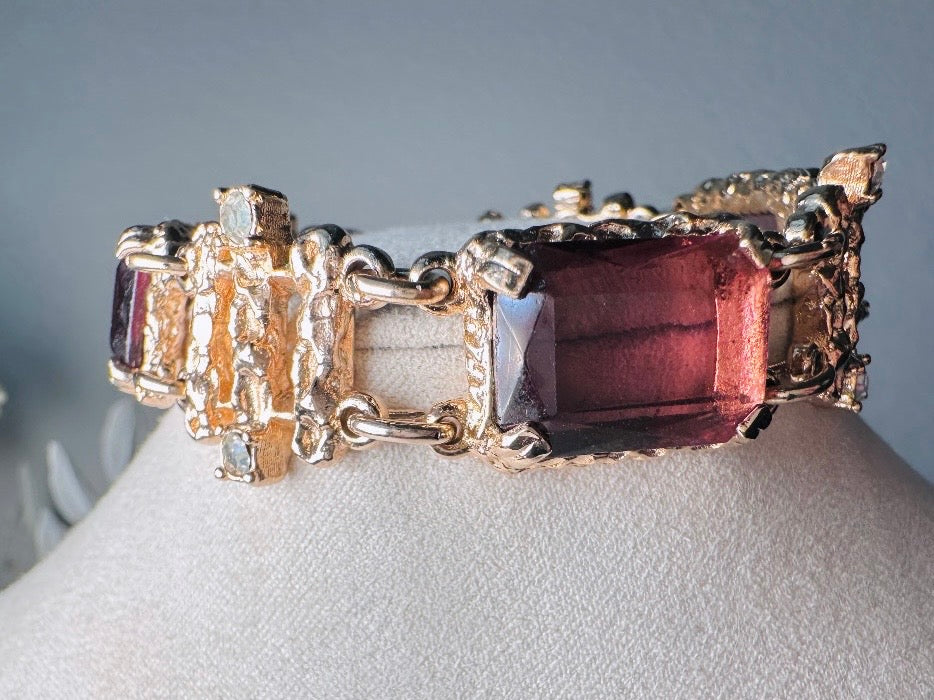 This 1970s faux amethyst vintage statement bracelet is gorgeous. Featuring three large smoky purple amethyst emerald cut stones prong set in gold. The setting is absolutely gorgeous in it's molten details- with a framed backing so the light can reflect through. Between each stone are golden branches in a brutalist style with small crystal accents. Absolutely beautiful vintage piece. Marked Sarah Coventry from 1973 Twilight collection.