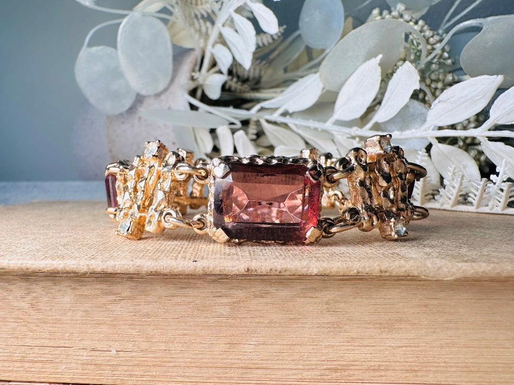 This 1970s faux amethyst vintage statement bracelet is gorgeous. Featuring three large smoky purple amethyst emerald cut stones prong set in gold. The setting is absolutely gorgeous in it's molten details- with a framed backing so the light can reflect through. Between each stone are golden branches in a brutalist style with small crystal accents. Absolutely beautiful vintage piece. Marked Sarah Coventry from 1973 Twilight collection.