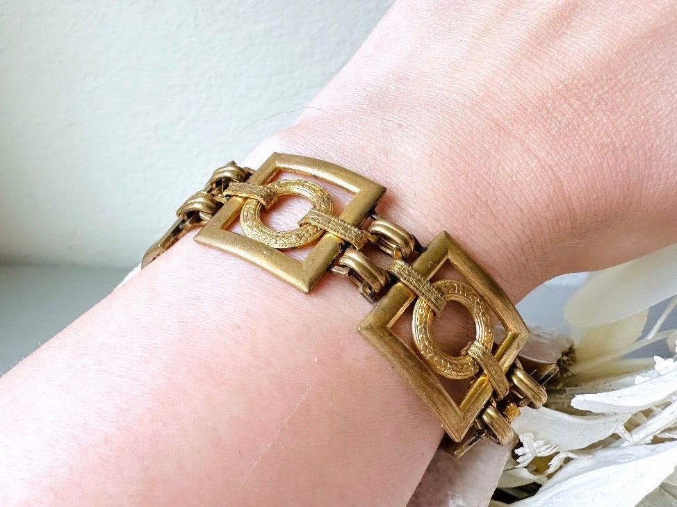 This is a vintage square link bracelet composed of antique gold geometric links. Featuring five structured squares with a floral embossed circle ring inside each one. This bold 1970s vintage chain bracelet is so unique; the circle inside of square and contrast of the bold shape with the royal floral motif is so interesting. It is 7 inches long in great vintage condition. Worn on wrist for size reference.