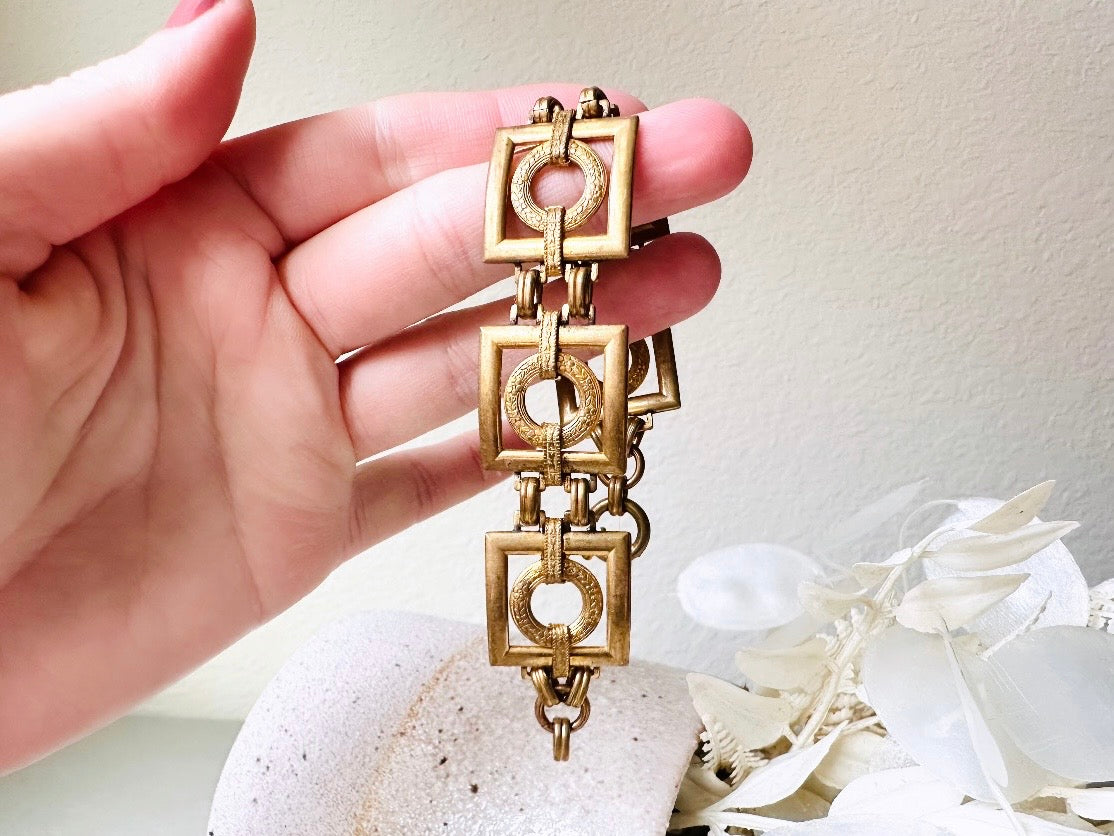 This is a vintage square link bracelet composed of antique gold geometric links. Featuring five structured squares with a floral embossed circle ring inside each one. This bold 1970s vintage chain bracelet is so unique; the circle inside of square and contrast of the bold shape with the royal floral motif is so interesting. It is 7 inches long in great vintage condition.