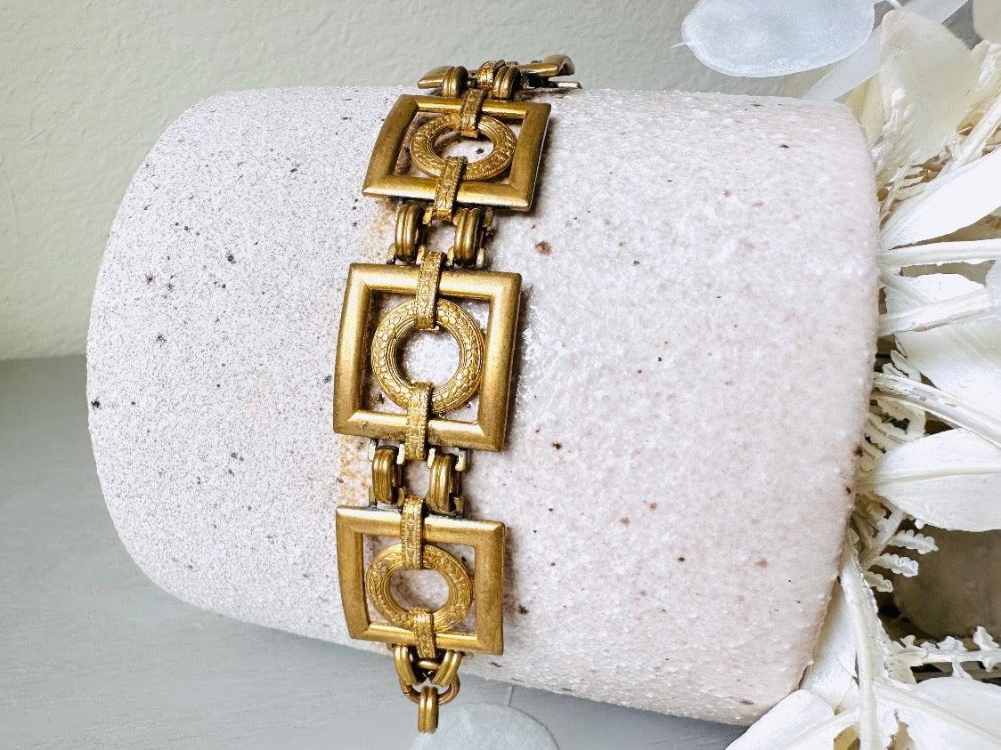 This is a vintage square link bracelet composed of antique gold geometric links. Featuring five structured squares with a floral embossed circle ring inside each one. This bold 1970s vintage chain bracelet is so unique; the circle inside of square and contrast of the bold shape with the royal floral motif is so interesting. It is 7 inches long in great vintage condition.