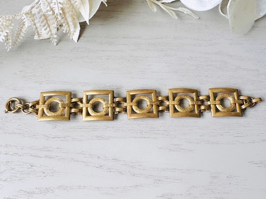 This is a vintage square link bracelet composed of antique gold geometric links. Featuring five structured squares with a floral embossed circle ring inside each one. This bold 1970s vintage chain bracelet is so unique; the circle inside of square and contrast of the bold shape with the royal floral motif is so interesting. It is 7 inches long in great vintage condition.