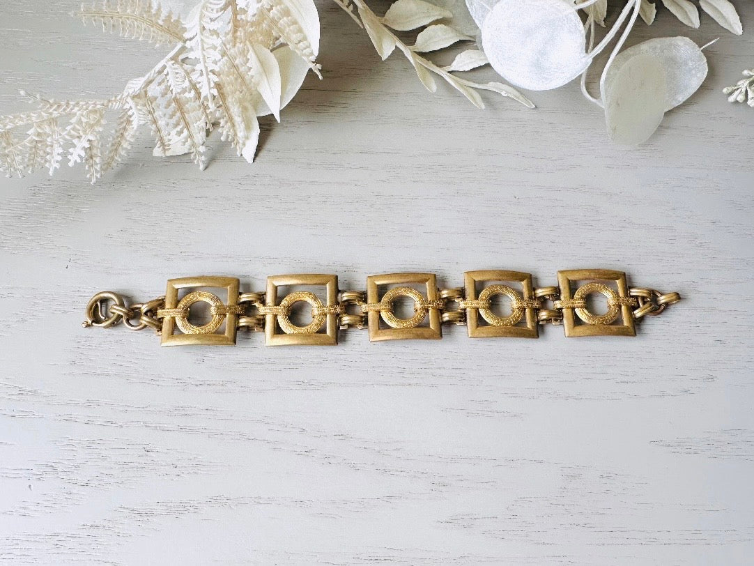 This is a vintage square link bracelet composed of antique gold geometric links. Featuring five structured squares with a floral embossed circle ring inside each one. This bold 1970s vintage chain bracelet is so unique; the circle inside of square and contrast of the bold shape with the royal floral motif is so interesting. It is 7 inches long in great vintage condition.