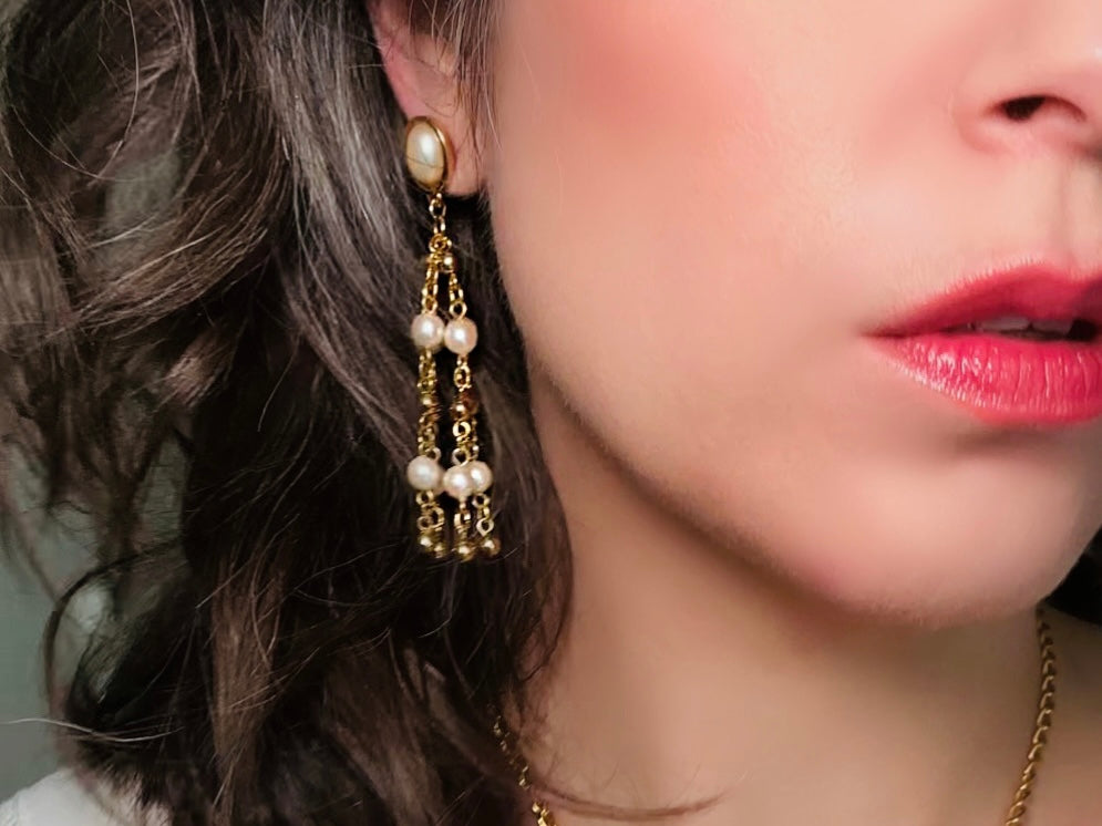 A pair of elegant vintage Trifari pearl chandelier earrings from the 1980s. These signed Trifari designer vintage earrings feature a cream pearl oval framed in gold as the post with a cascade of delicate long fine gold chain tassels with pearl links. In excellent vintage condition, they are three inches long.