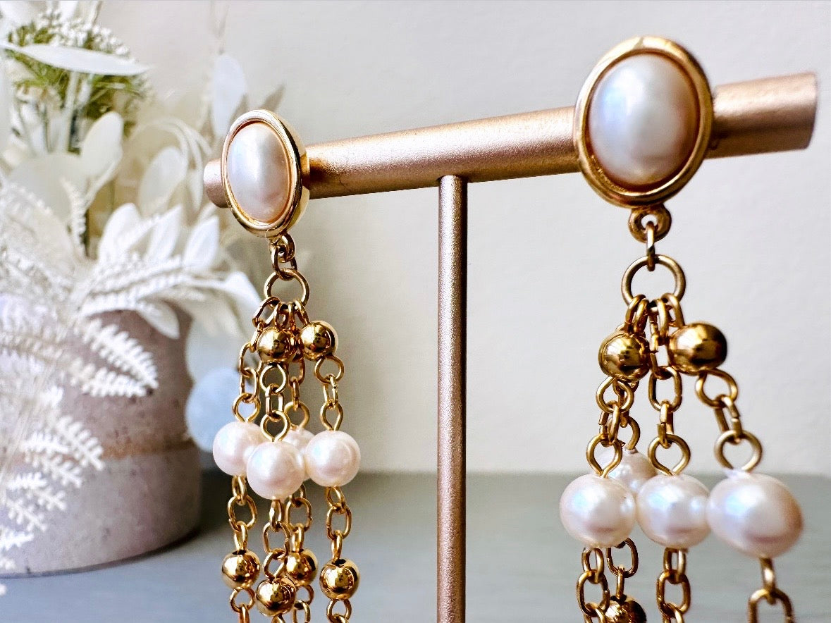 A pair of elegant vintage Trifari pearl chandelier earrings from the 1980s. These signed Trifari designer vintage earrings feature a cream pearl oval framed in gold as the post with a cascade of delicate long fine gold chain tassels with pearl links. In excellent vintage condition, they are three inches long.