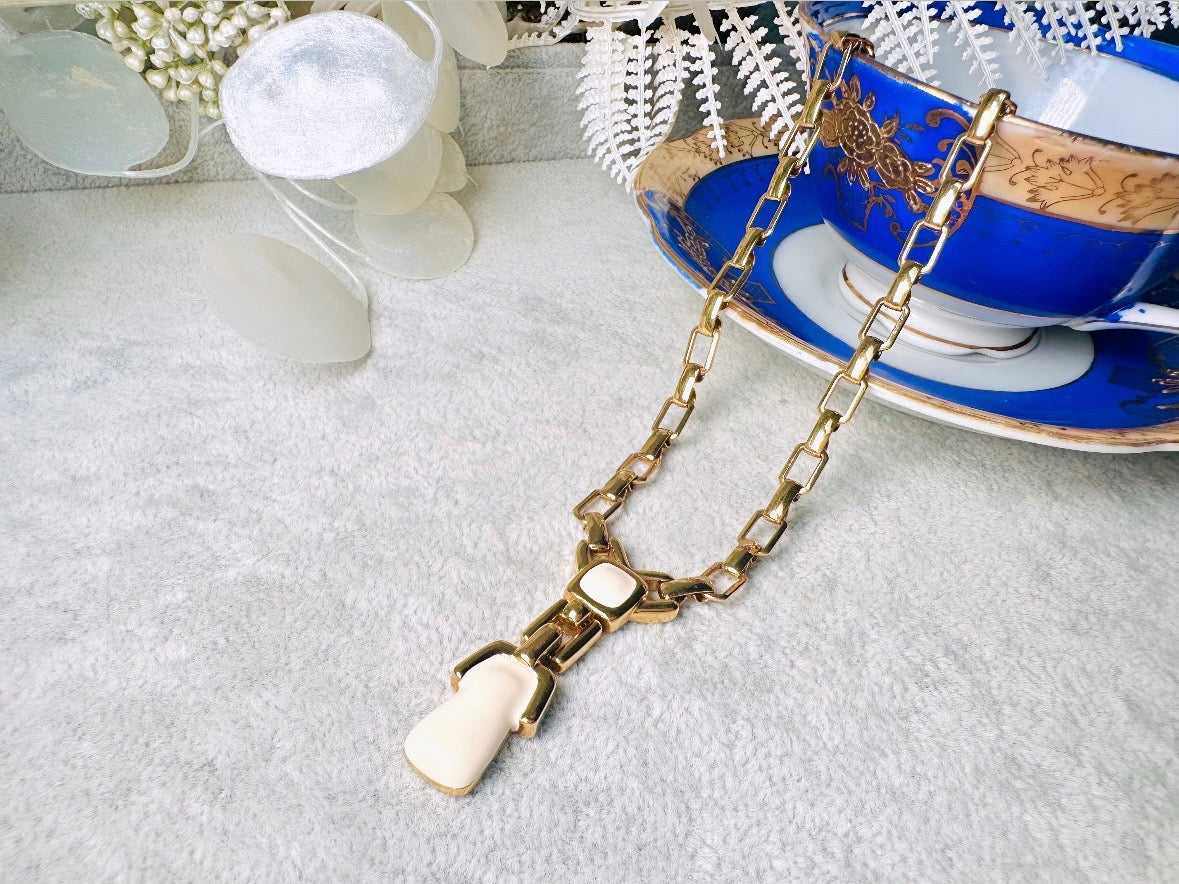 This vintage gold chain Y necklace by Monet is a rare find. Featuring flat link cable chain with a geometric drop pendant with cream enamel accents. This signed vintage necklace is from the 1970s at a peak time for Monet designs. This classic necklace is in excellent condition and just as classic today as it was when it debuted. Adjustable length with a hook closure. 