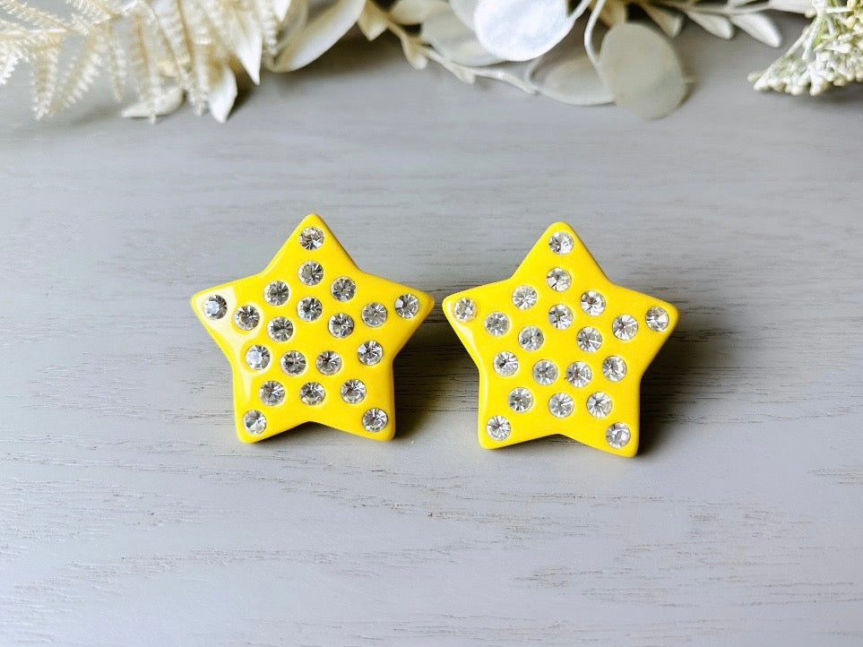A pair of yellow star earrings from Piggle and Pop. A highly collectible pair of 1980s statement earrings. These yellow star earrings are bright banana yellow opaque lucite with diamond rhinestone accents. Huge vintage star clip ons with major rockstar vibes.