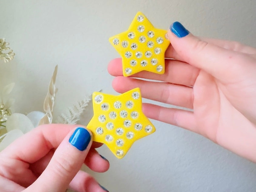 A pair of yellow star earrings from Piggle and Pop. A highly collectible pair of 1980s statement earrings. These yellow star earrings are bright banana yellow opaque lucite with diamond rhinestone accents. Huge vintage star clip ons with major rockstar vibes.