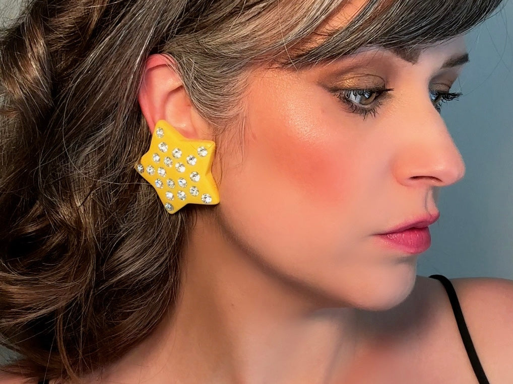 A pair of yellow star earrings from Piggle and Pop. A highly collectible pair of 1980s statement earrings. These yellow star earrings are bright banana yellow opaque lucite with diamond rhinestone accents. Huge vintage star clip ons with major rockstar vibes. Modeled for size reference.