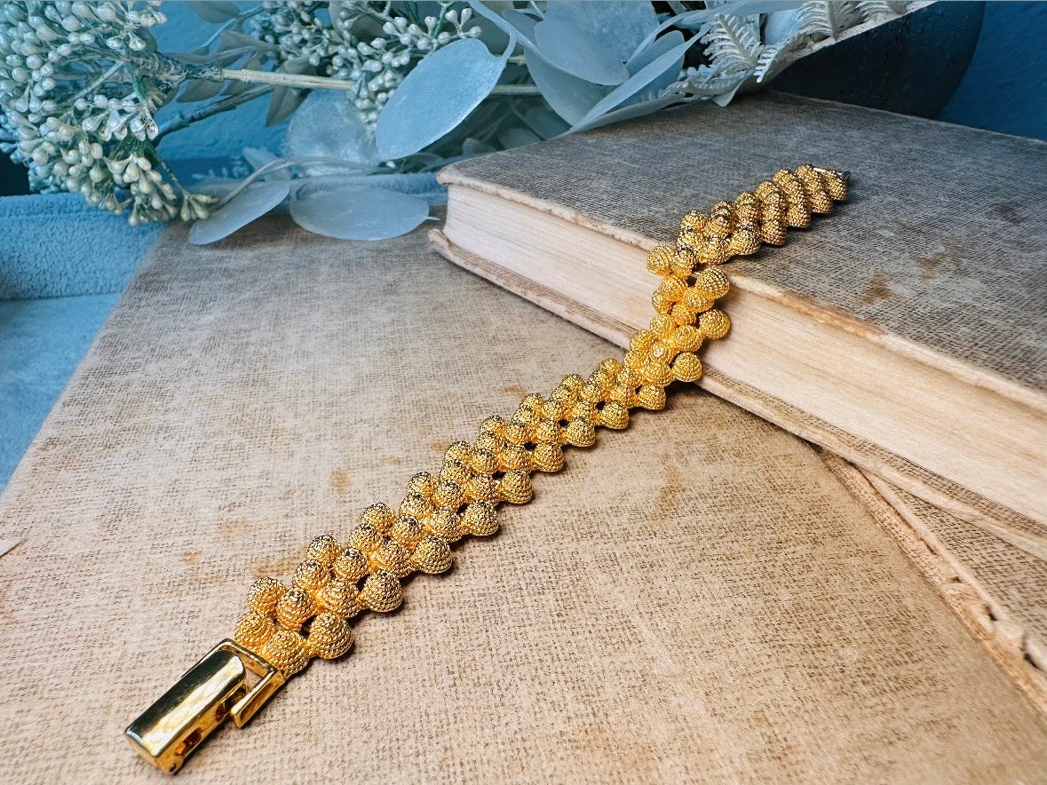 Gold bracelet on a textured surface with a book and decorative leaves in the background