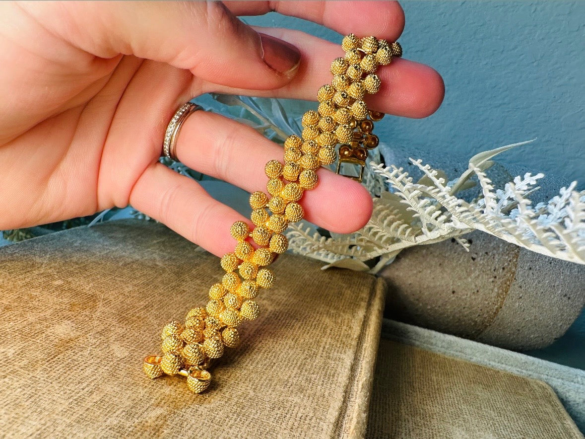 vintage Gold beaded bracelet held by a hand on a textured surface with a neutral background
