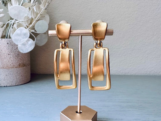 These Anne Klein vintage matte gold designer earrings are spectacular. Full of 1980s bold glamour, these clip ons have a satin gold finish and a geometric design. These vintage dangle earrings are bold and elegant, with curved square posts and rectangular drops with a cut out hollow border. These are big and incredibly well made in a satin matte gold finish. Clip on style, easy to wear and in great vintage condition. Highly sought after designer vintage. 