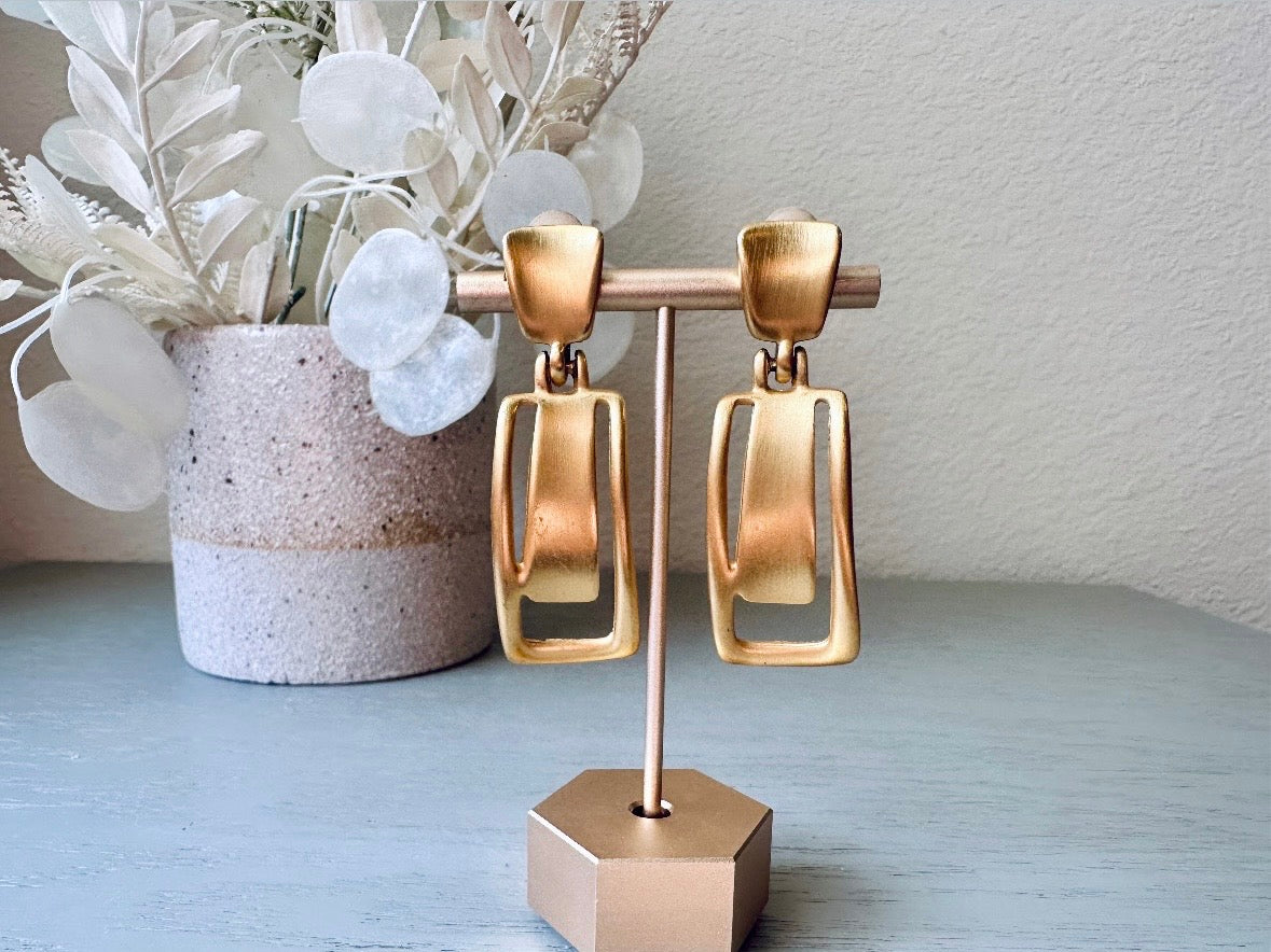 These Anne Klein vintage matte gold designer earrings are spectacular. Full of 1980s bold glamour, these clip ons have a satin gold finish and a geometric design. These vintage dangle earrings are bold and elegant, with curved square posts and rectangular drops with a cut out hollow border. These are big and incredibly well made in a satin matte gold finish. Clip on style, easy to wear and in great vintage condition. Highly sought after designer vintage. 