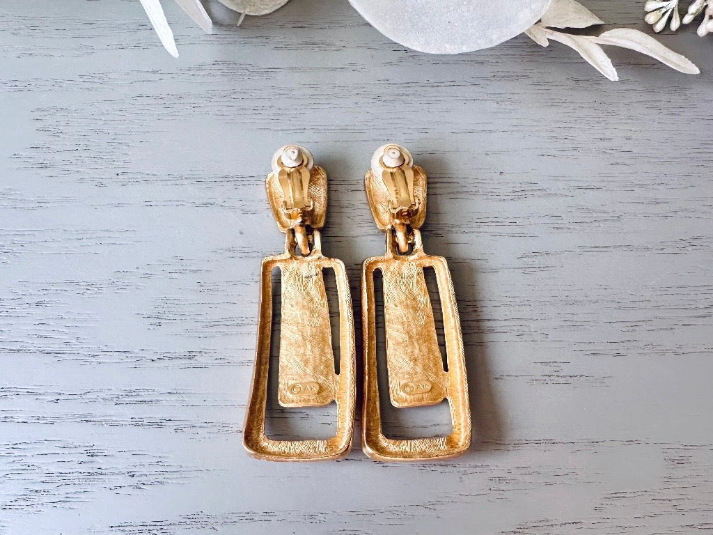 These Anne Klein vintage matte gold designer earrings are spectacular. Full of 1980s bold glamour, these clip ons have a satin gold finish and a geometric design. These vintage dangle earrings are bold and elegant, with curved square posts and rectangular drops with a cut out hollow border. These are big and incredibly well made in a satin matte gold finish. Clip on style, easy to wear and in great vintage condition. Highly sought after designer vintage. 
