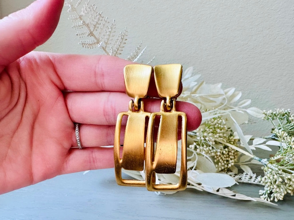 These Anne Klein vintage matte gold designer earrings are spectacular. Full of 1980s bold glamour, these clip ons have a satin gold finish and a geometric design. These vintage dangle earrings are bold and elegant, with curved square posts and rectangular drops with a cut out hollow border. These are big and incredibly well made in a satin matte gold finish. Clip on style, easy to wear and in great vintage condition. Highly sought after designer vintage. 