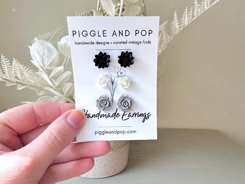 This lovely flower stud earring set of monochromatic flowers is a classic staple for any jewelry box! This floral post earring set features one pair of black lotus earrings, one pair of white rose studs and one pair of matte grey open rose earrings. They are made with glossy resin and hypoallergenic surgical steel posts.