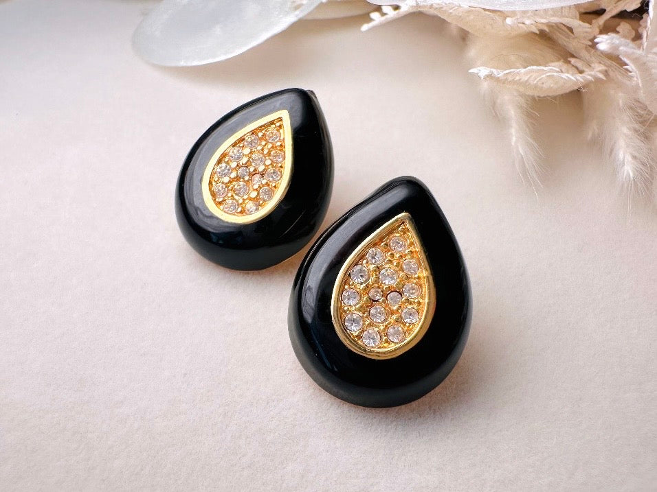 Black teardrop-shaped earrings with gold and crystal details on a light background