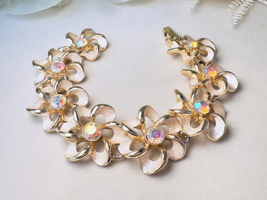 A gold-tone floral bracelet with iridescent rhinestones, displayed on a light beige surface.