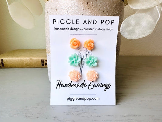 This flower stud earring set features a gorgeous combination of peach and mint stud earrings. This set features light sorbet orange roses, minty aqua lotus earrings and light peach open rose studs. These pretty flower earrings have hypoallergenic surgical steel posts with butterfly backs making them great for everyday + all day wear.