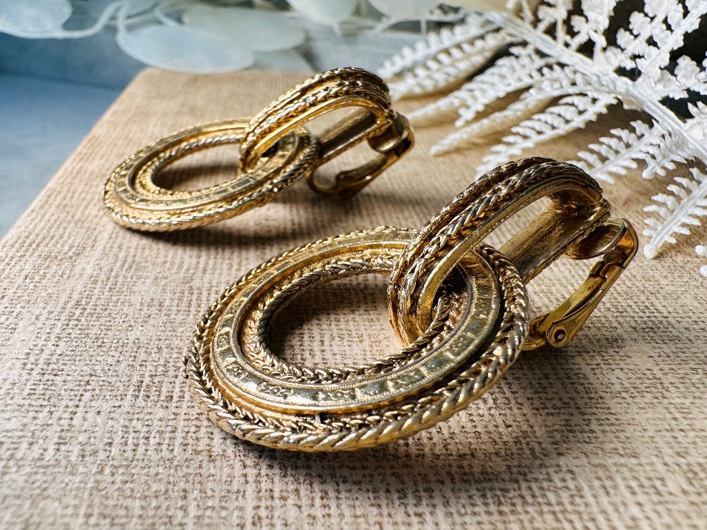 These vintage gold door knocker earrings are absolutely fabulous! Gold tone door knocker style hoops &nbsp;are chock full of interesting details. These earrings feature 3 rows of textured raised concentric hoops- the outer rings are a gold roped pattern and the center is rows of rectangle panels. These earrings are such a classic Etruscan pair- bold and dramatic! In great vintage condition -no major flaws to note- please see pics. Clip on style!

Dimensions: 1.5" x 1.25"&nbsp;