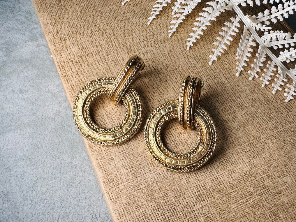 These vintage gold door knocker earrings are absolutely fabulous! Gold tone door knocker style hoops &nbsp;are chock full of interesting details. These earrings feature 3 rows of textured raised concentric hoops- the outer rings are a gold roped pattern and the center is rows of rectangle panels. These earrings are such a classic Etruscan pair- bold and dramatic! In great vintage condition -no major flaws to note- please see pics. Clip on style!

Dimensions: 1.5" x 1.25"&nbsp;