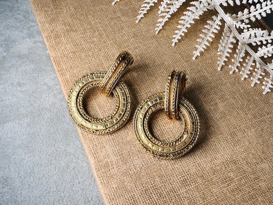 These vintage gold door knocker earrings are absolutely fabulous! Gold tone door knocker style hoops &nbsp;are chock full of interesting details. These earrings feature 3 rows of textured raised concentric hoops- the outer rings are a gold roped pattern and the center is rows of rectangle panels. These earrings are such a classic Etruscan pair- bold and dramatic! In great vintage condition -no major flaws to note- please see pics. Clip on style!

Dimensions: 1.5" x 1.25"&nbsp;