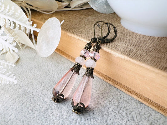 These beautiful Victorian earrings are handmade with rose quartz stones, lustrous pink Czech glass teardrop beads, and faceted crystals. These whimsical blushing rose earrings feature a delightful mix of soft pink hues and rustic bronze detailing. A wonderful pair of earrings for elegant everyday wear.