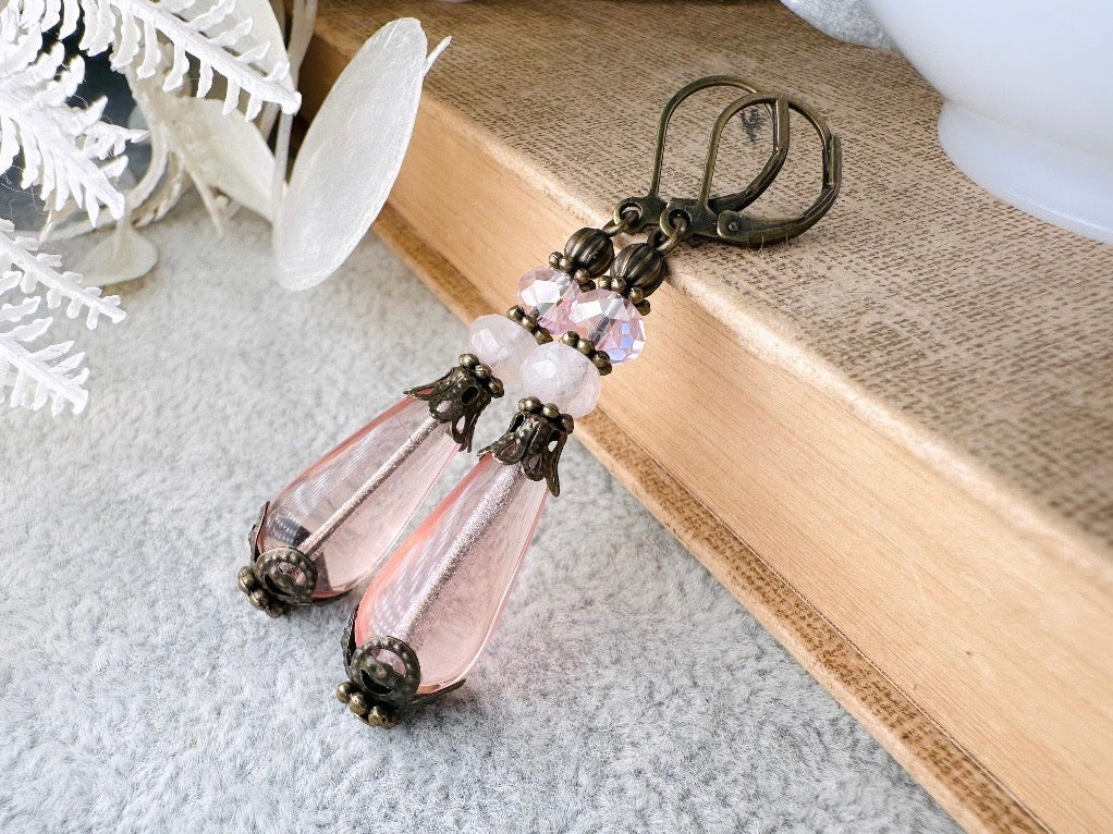 These beautiful Victorian earrings are handmade with rose quartz stones, lustrous pink Czech glass teardrop beads, and faceted crystals. These whimsical blushing rose earrings feature a delightful mix of soft pink hues and rustic bronze detailing. A wonderful pair of earrings for elegant everyday wear.